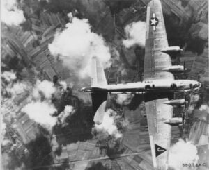 B-17 "Flying Fortress" airplane flies over a patchwork land with large puffs of smoke. 
